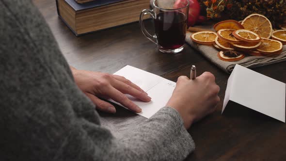 Woman Writes Christmas Greetings on a Greeting Card. Close Up