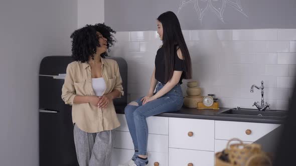 Two Young Female Friends Standing in Kitchen Gossiping