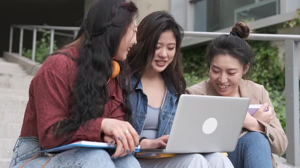 Group of Asian female students using a laptop and studying together on the stair