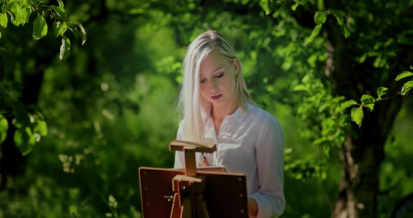 Portrait of a Young Beautiful Woman Painting in the Garden Sunny Day and Around Green Trees