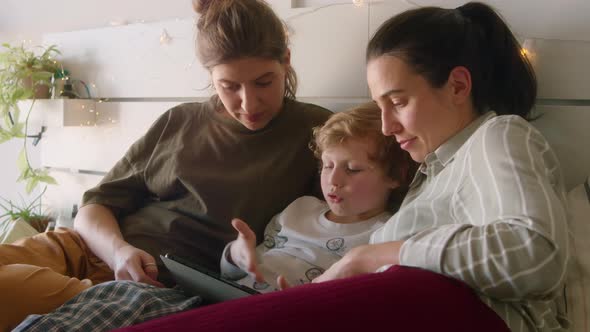 Kid Using Tablet and Chatting with Lesbian Mothers in Bedroom