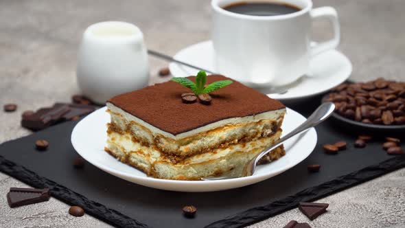 Portion of Traditional Italian Tiramisu dessert and cup of coffee on grey concrete background