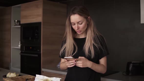 Shot of Young Woman Using Her Mobile Phone in the Kitchen at Home in the Morning
