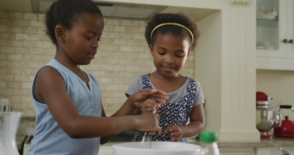 Happy two african american girls baking and mixing ingredients in kitchen