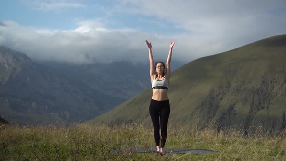 Young Woman in Tracksuit Practices Yoga Performing Mountain Pose in the Mountains.