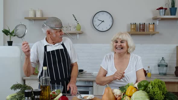 Happy Senior Couple Dancing While Cooking Together in Kitchen with Fresh Vegetables and Fruits