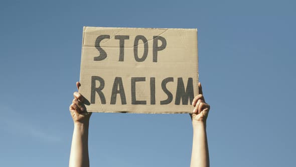 Woman hands hold poster Stop Racism. Sign "Stop Racism"against blue sky.
