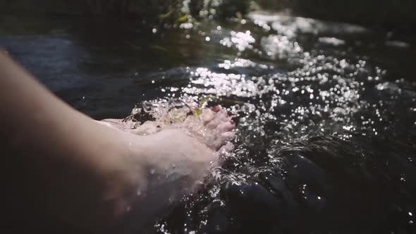 Woman Relaxes By River Sitting on Edge of Rock Swing One's Feet on Water Flow