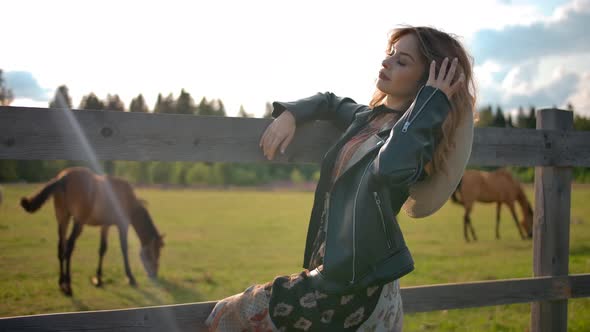 Elegant Female Resting Near Grazing Horses on Farm