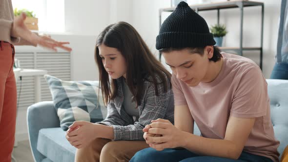 Unhappy Teenagers Brother and Sister Sitting on Couch While Parents Yelling Punishing Kids at Home