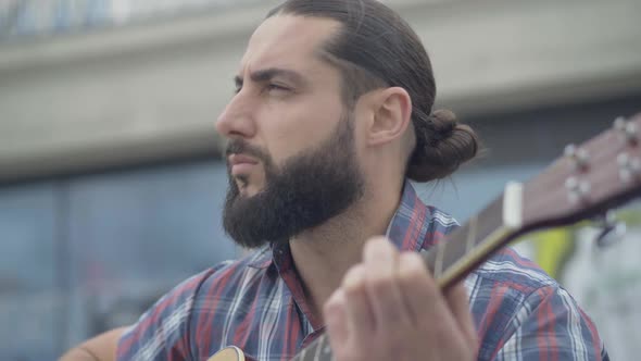 Close-up Portrait of Engrossed Caucasian Musician Playing Guitar Outdoors. Handsome Absorbed Man