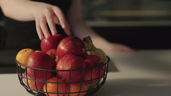 Woman Reaching For Ripe Red Apple From Fruit Bowl In Kitchen