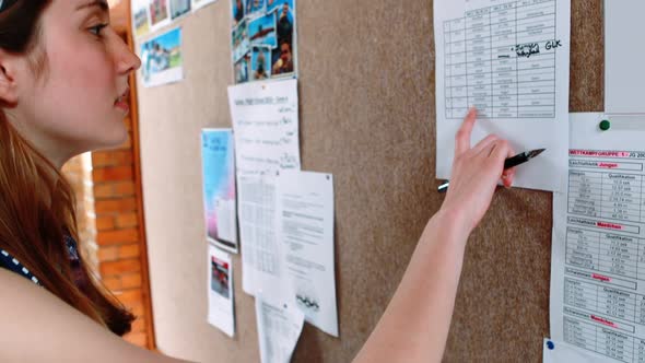 Smiling schoolgirl reading notice board in corridor