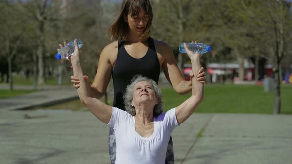 Concentrated Senior Woman Doing Exercises with Trainer in Park