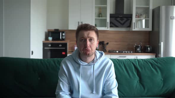 Sad Guy Sitting on the Couch in the Living Room Looking at the Camera