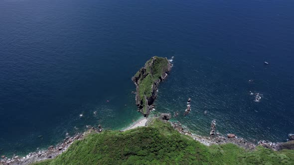 Aerial view straight down a steep cliff towards small island in deep blue water along highway 9 in E