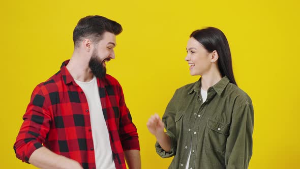 Portrait of a Young Couple Making High Five and Smiling at Camera in Yellow Studio