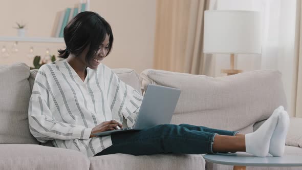 Young Woman Relaxing at Home on Cozy Sofa with Laptop Chatting with Friends in Social Network