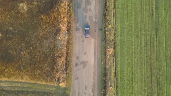 Top down aerial view of a car driving fast on bad road with potholes.