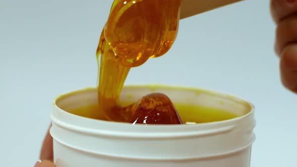 Beautician removes sugar paste from a white jar with a wooden spatula before the sugaring procedure