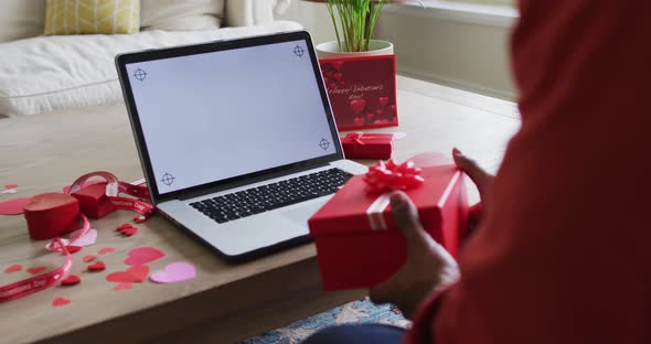 Midsection of biracial man holding present and having valentine's video call on laptop