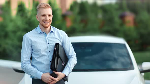 Portrait of Successful Smiling Young Business Man Holding Briefcase Posing at White Car Background