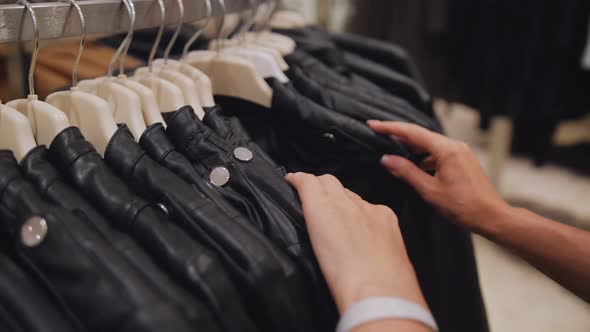 Closeup of Women's Hands in a Clothing Store Choosing a Leather Jacket on Hangers