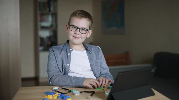 Boy in Glasses Sits at Table Looks at Camera Smiles Makes Faces