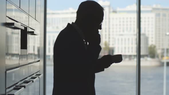 Senior Businessman Talking on Mobile Phone Taking Coffee From Automated Machine in Office Kitchen