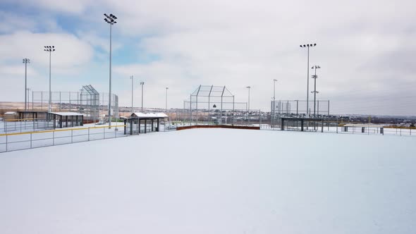 Baseball and softball field covered in fresh powder snow during the day, aerial orbit