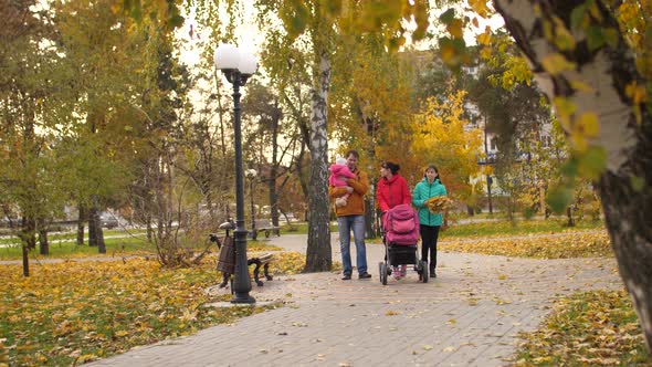 Happy Parents with a Small Baby and an Adult Daughter Walk in the Autumn Park and Laugh. Mom and Dad