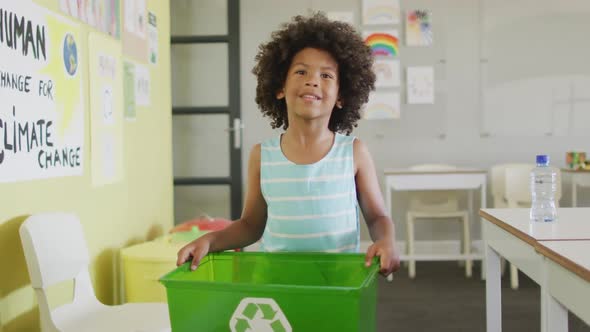 Video of happy african american boy holding box with recycling symbol in classroom