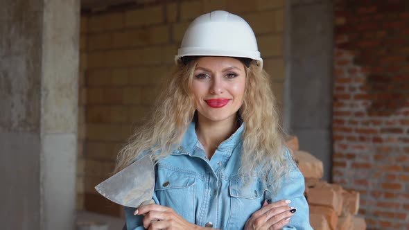 A Female Builder in a Helmet and Denim Work Uniform Stands on a Construction Site