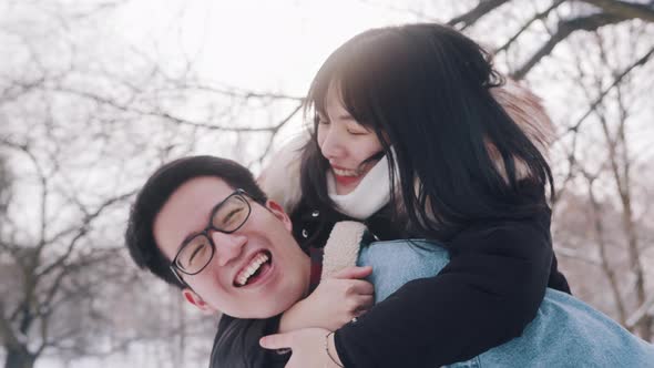 Young Man Giving Piggyback Ride To His Girlfriend in the Park on Snowy Winter Day