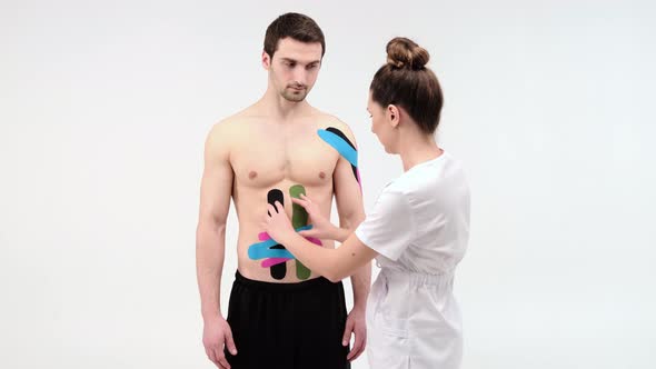 Female therapist applying kinesiology tape on a man's abdomen. Woman prepares male patient