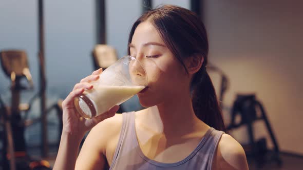 Attractive fitness asian woman finishing workout and drinking protein milk shake vitamins