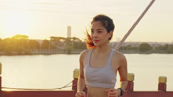 Asian young beautiful woman running for health in the evening sunset on the bridge in public park.