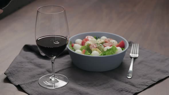 Slow Motion Pour Red Wine Into Wineglass with Bowl of Salad on Background
