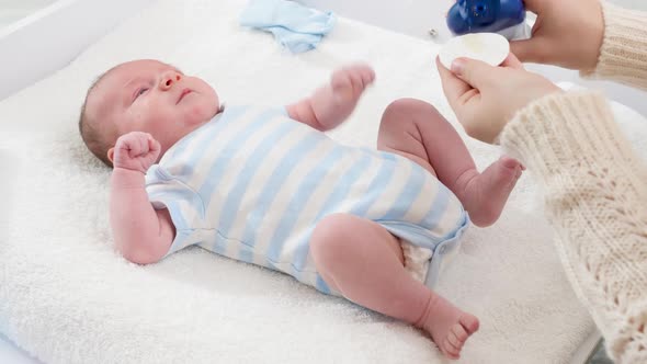 Young Caring Mother Applying Baby Oil for Moisturizing Soft Sking of Her Newborn Baby Son Lying on