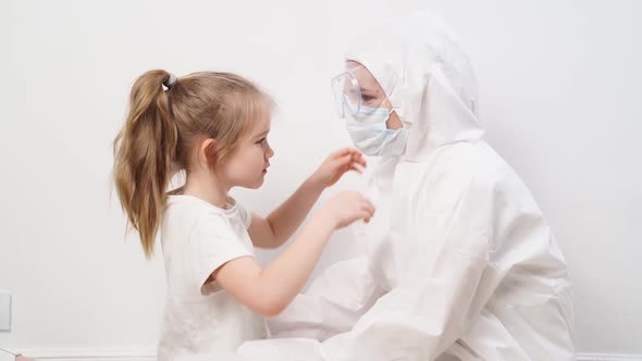 A Little Girl Hugs a Doctor in a White Protective Suit Mask Glasses and Gloves