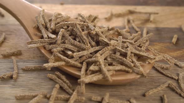 Wheat rye bran flakes sticks fall on a wooden spoon in slow motion