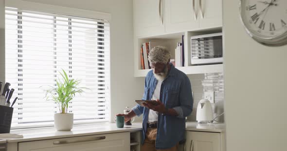Video of african american senior man drinking coffee and using tablet