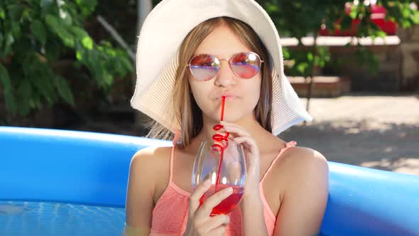 Portrait of Beautiful Young Girl Drinking Cocktail and Splashing Water in Outdoor Swimming Pool at