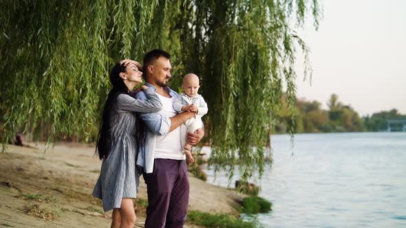 Loving Family with Baby Standing on River Bank