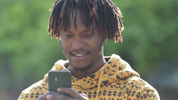 Young Happy Handsome African Man Smiling While Using Phone in the Streets Outdoors