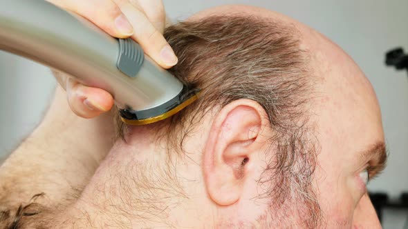 Man shaves his head. An overgrown man with a bald patch clumsily cuts his brown gray hair on his