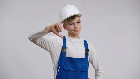 Sad Dissatisfied Caucasian Boy Showing Thumb Down Posing in Builder Uniform at White Background