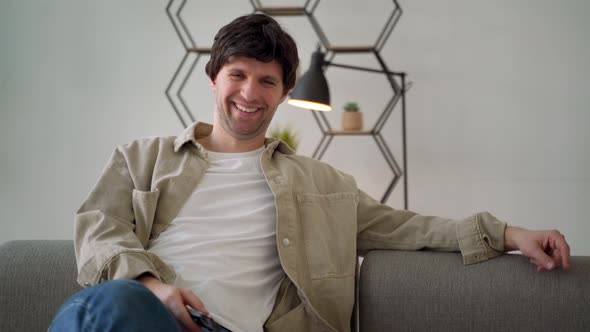 Young Man Holding Television Remote Control Smiling and Laughing Hard Out Loud