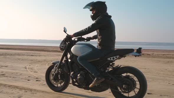 Motorcyclist Driving His Customized Fast Motorbike on the Dirt Road in Desert Around Sea or Lake