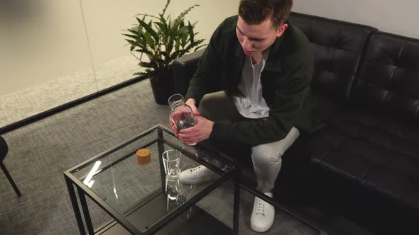 Attractive Man Pouring Water Into Glass In his living room watching the tv, television